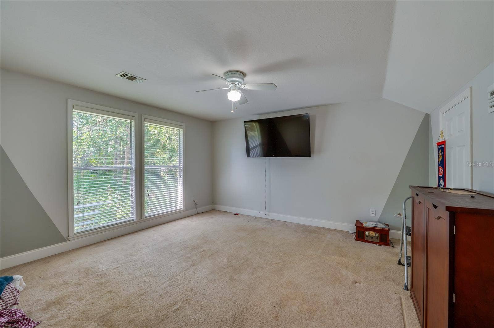 Spacious carpeted room featuring a white ceiling fan and large windows providing natural light.