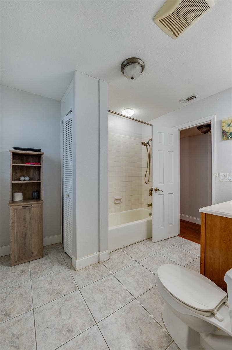 Tiled bathroom space highlighting a shower-tub combination, a white paneled interior door, and built-in closet storage.