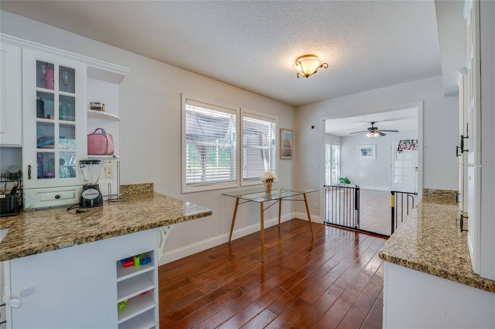 Functional kitchen nook featuring granite countertops, white cabinetry with display shelving, and rich laminate flooring.