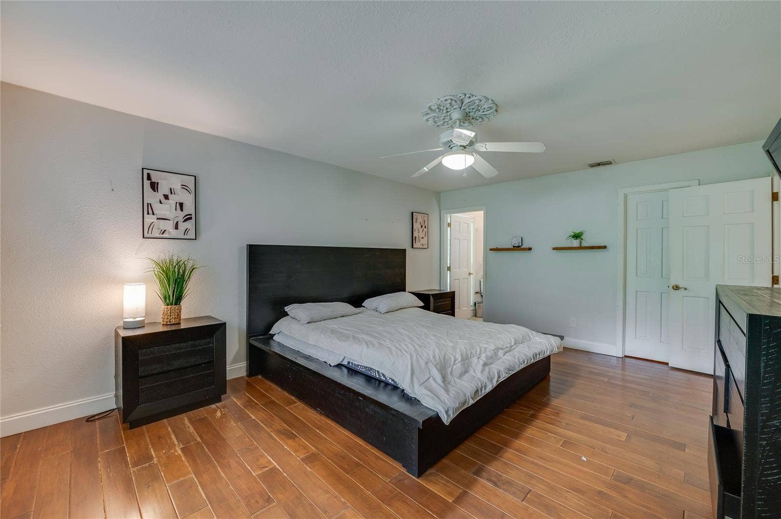 Comfortable master suite boasting rich laminate flooring, a central ceiling fan with ornate medallion molding, and direct access to an ensuite bathroom.