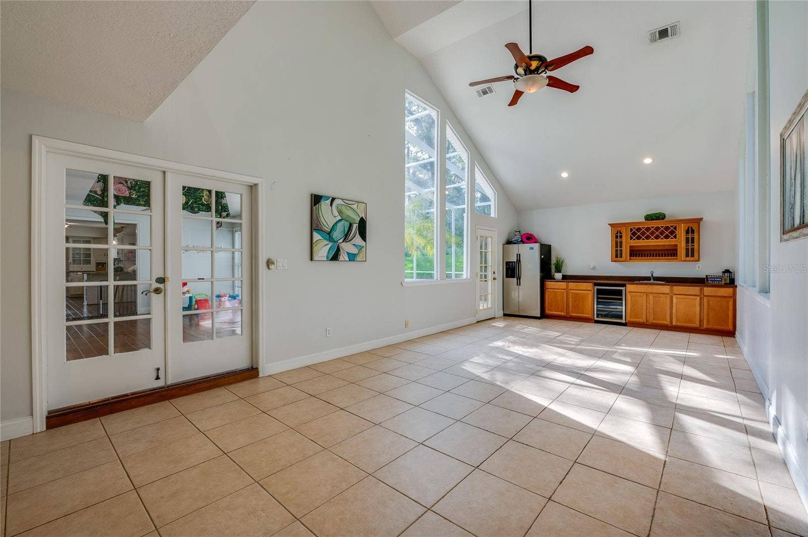 Bright multipurpose living space with soaring vaulted ceilings, skylight-style windows, ceramic tile flooring, and classic French doors.