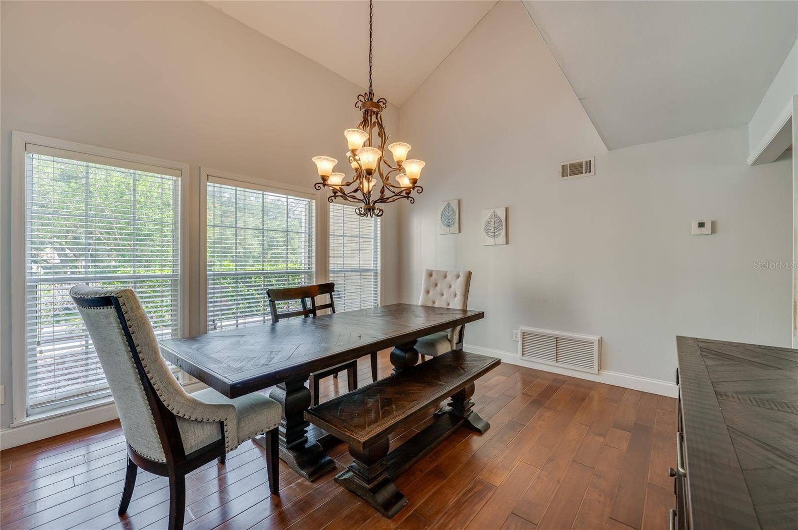 Formal dining area framed by vaulted ceilings and expansive windows, lit by an ornate iron chandelier over rich laminate floors.