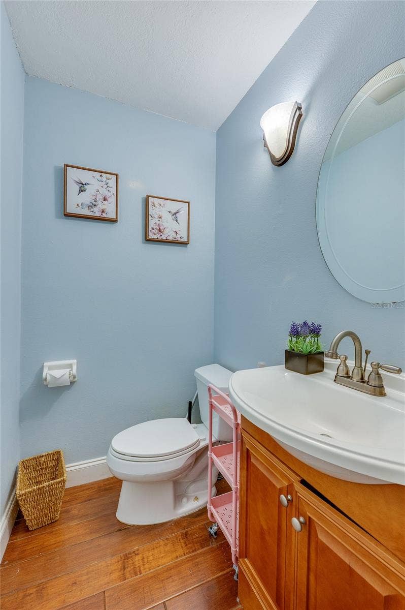 Charming half-bath featuring soft blue walls, a wooden vanity cabinet, oval mirror, and warm laminate flooring.