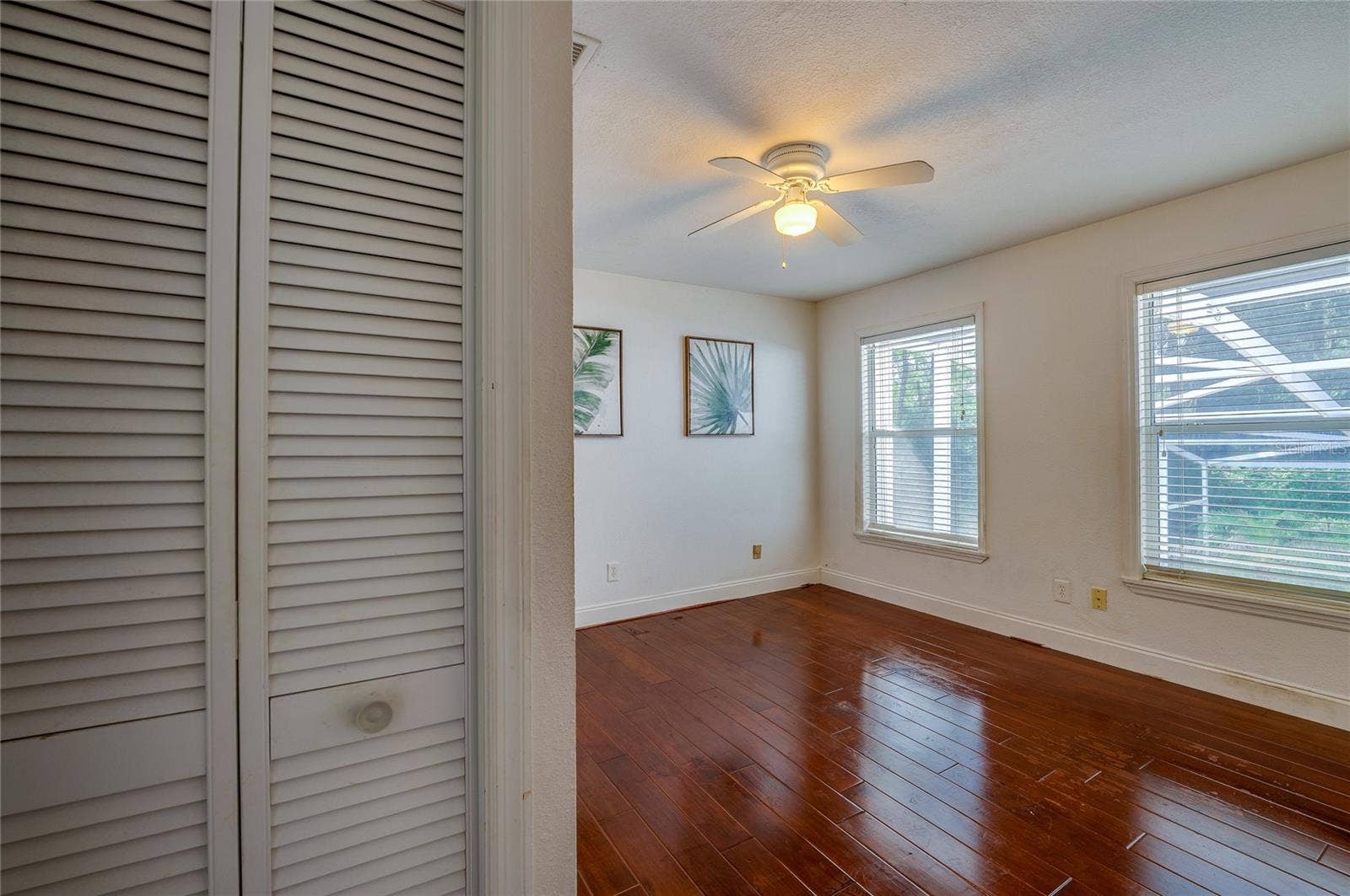 Sunlit bedroom space featuring rich laminate flooring, white wall trim, dual multi-pane windows, and a central ceiling fan.