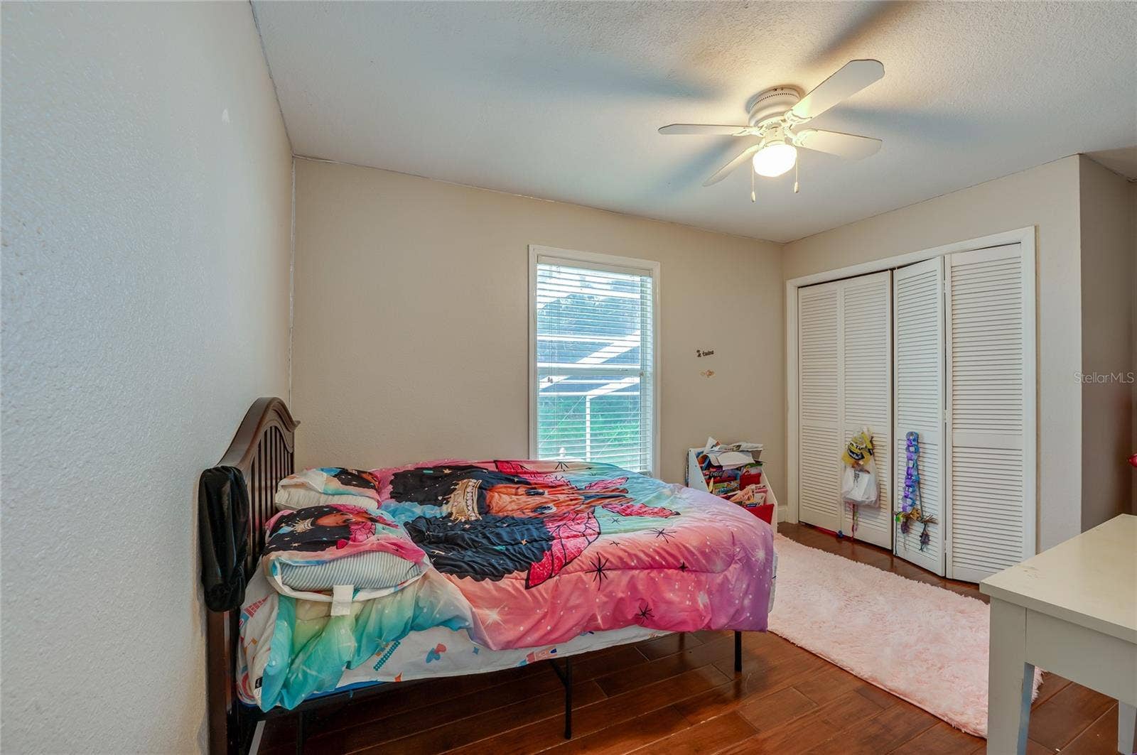 Cozy bedroom layout showcasing rich laminate floors, a central ceiling fan, and spacious closet doors.