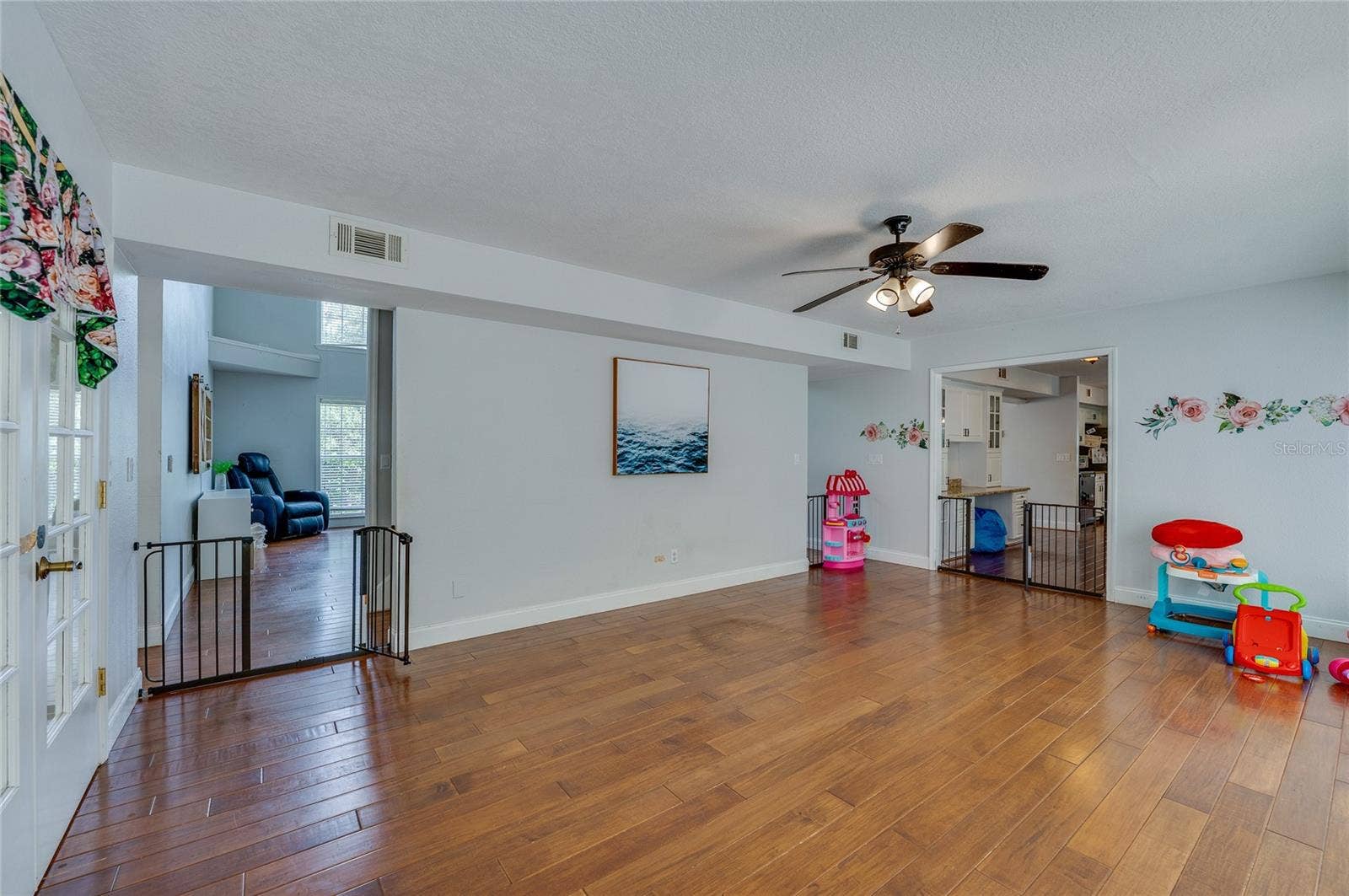 Versatile open room with rich laminate floors, a ceiling fan, and wide archway entrances connecting to surrounding living spaces.