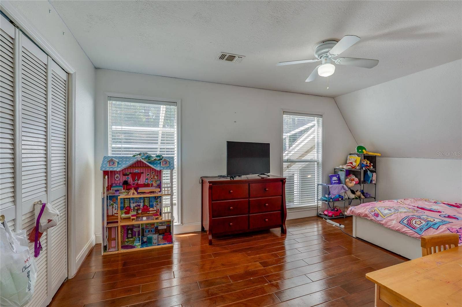 Versatile bedroom space showing warm laminate floors, white closet doors, and natural light from wide windows.