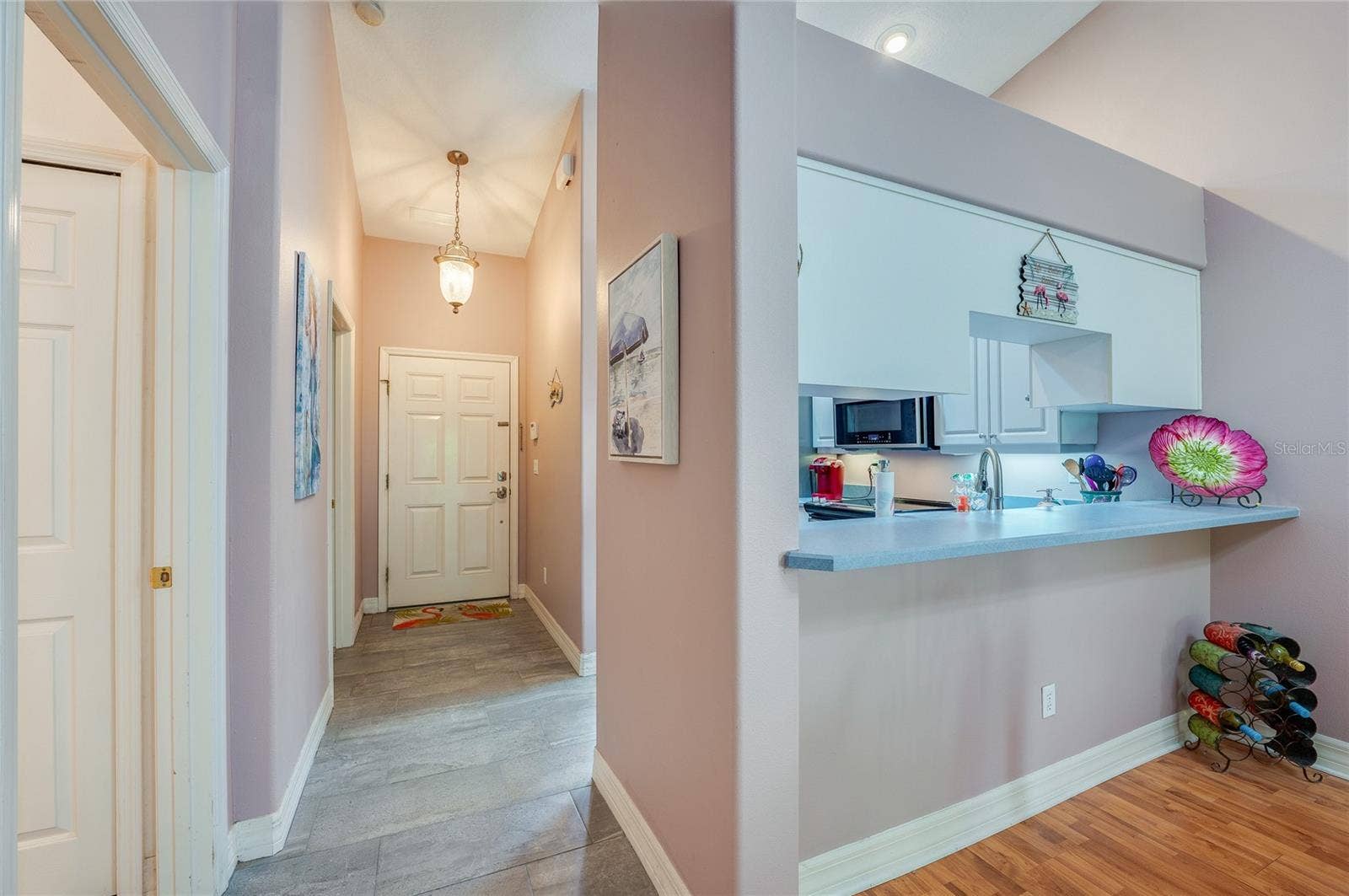 Welcoming home entrance featuring light grey tile flooring, soft purple walls, and a hanging light fixture. A raised breakfast bar overlooks the foyer, creating an open-concept flow.
