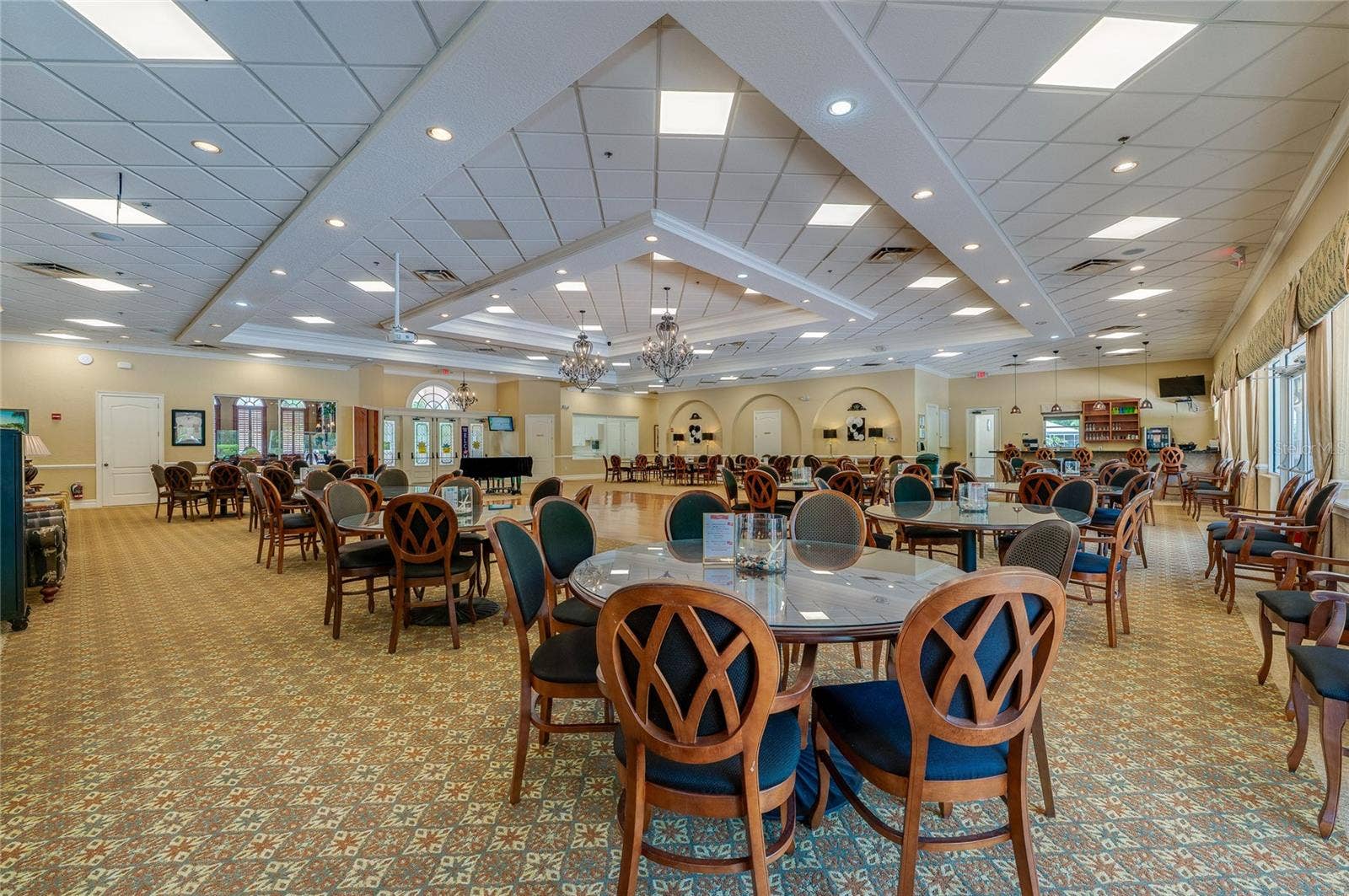 Wide perspective of the ballroom highlighting geometric drop ceilings, integrated lighting, and patterned carpeting that extends across the floor. Arched architectural elements and curtained glass doors line the perimeter walls.