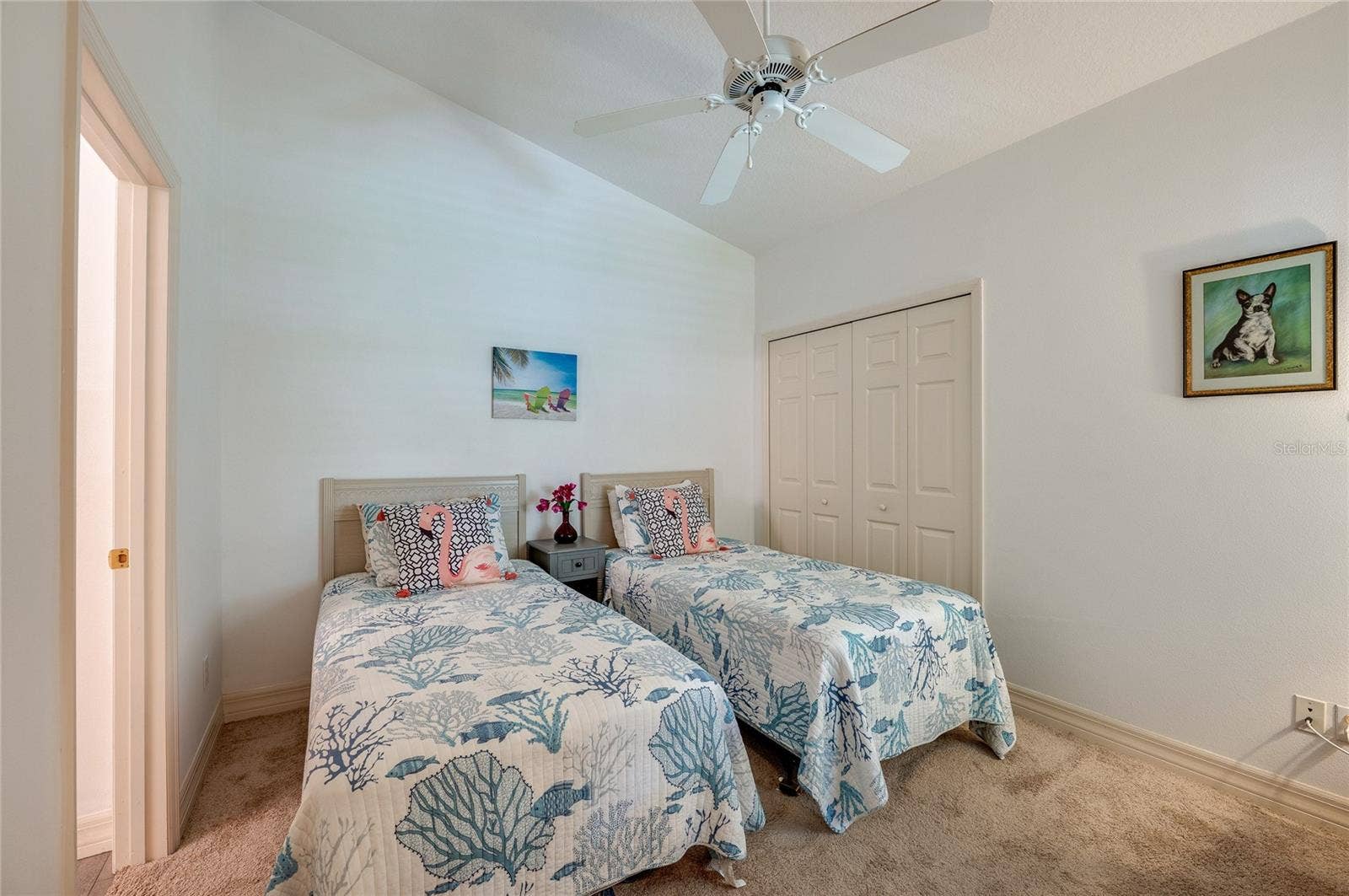 Bright bedroom showcasing vaulted ceilings, plush neutral carpeting, and a white ceiling fan. A bi-fold closet door accentuate the clean, airy layout.