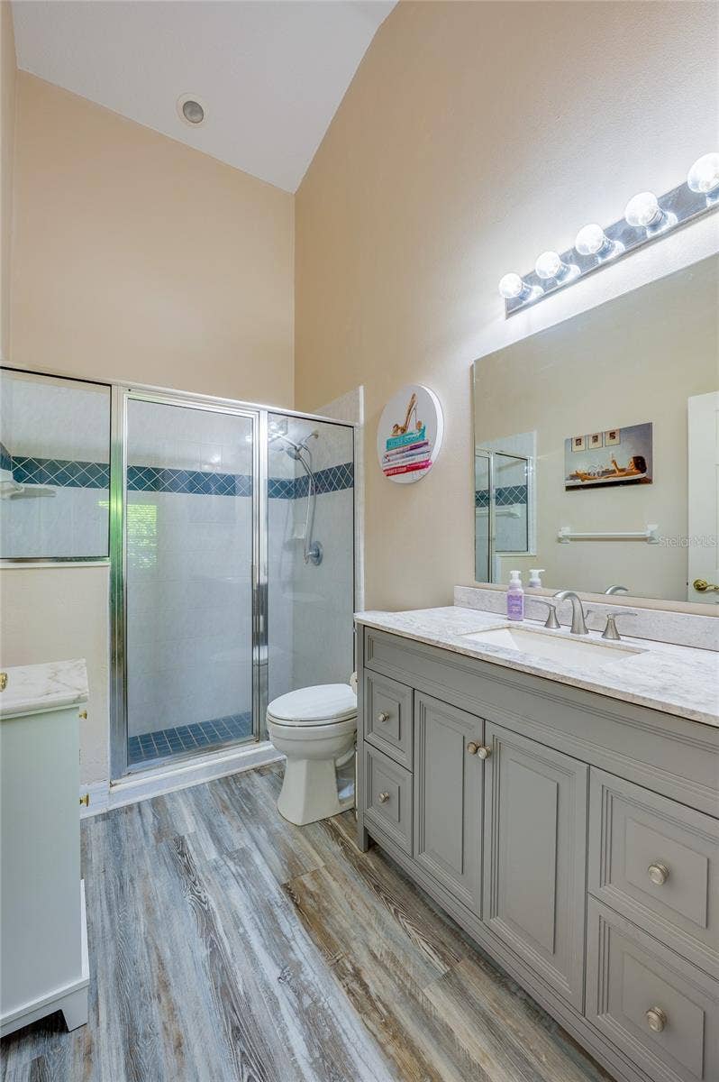 En-suite bathroom featuring a grey vanity with marble counter, modern laminate flooring, and vanity lighting. A glass-enclosed walk-in shower with decorative blue accent tile completes the space.