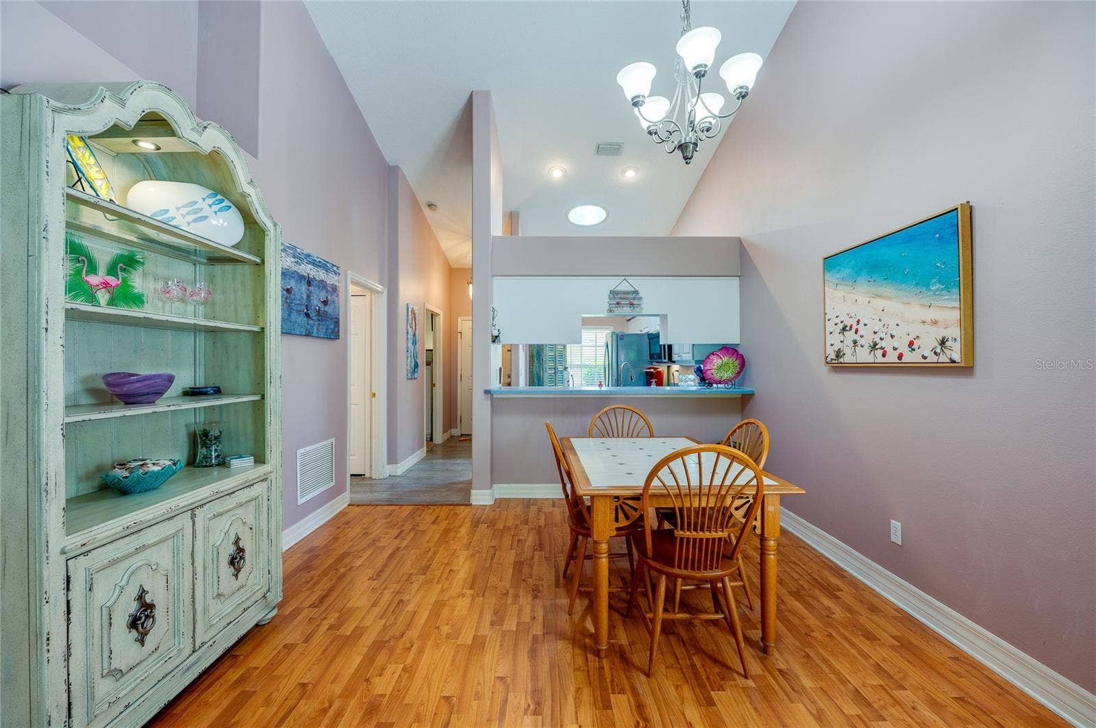 Open dining space featuring rich laminate flooring, high vaulted ceilings, and a central chandelier. A cutout wall provides a direct view into the kitchen, enhancing the overall flow.