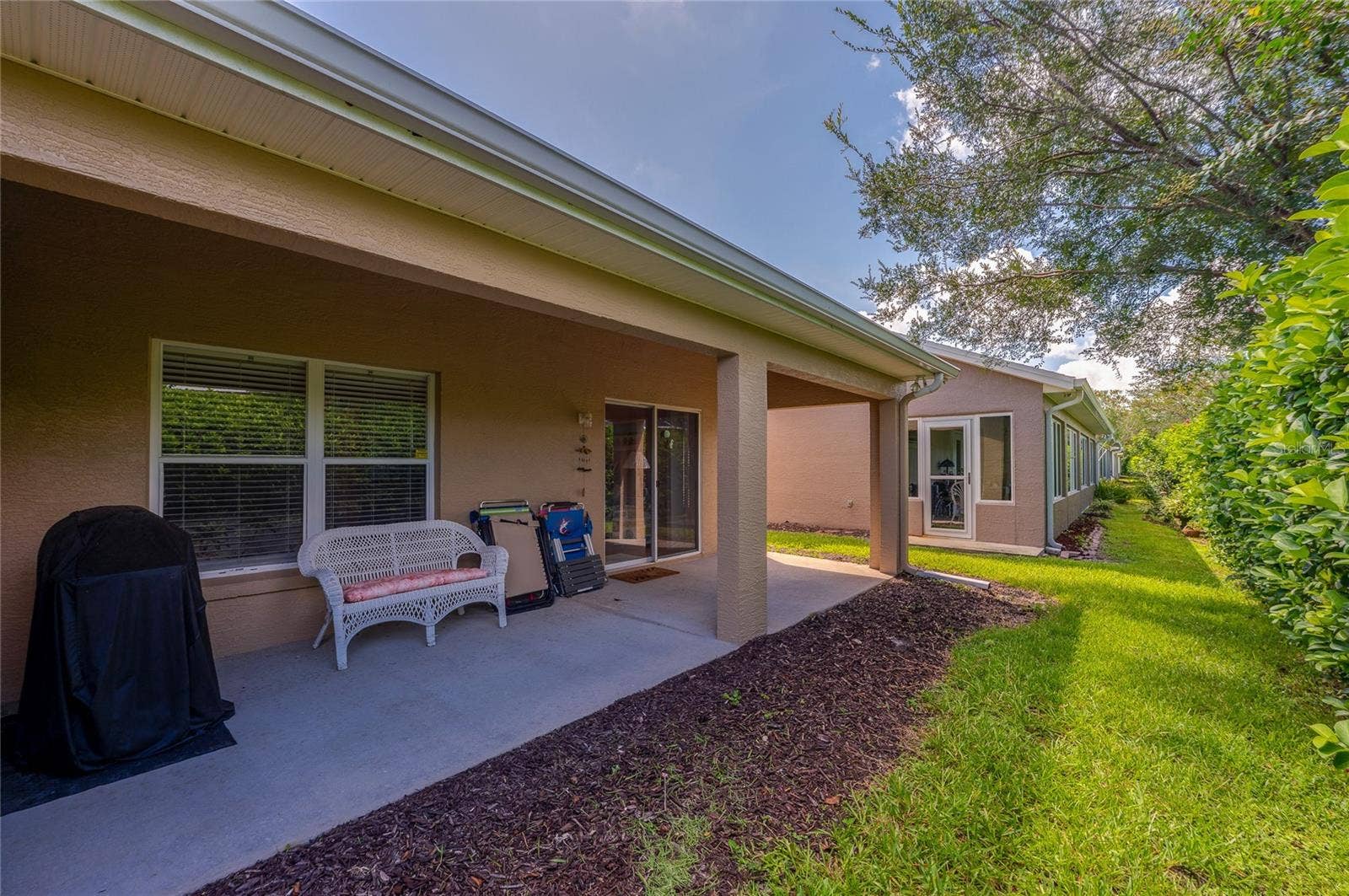 Sheltered back patio with concrete flooring leading out to a lush lawn area. Large glass sliding doors and windows provide easy indoor-outdoor flow along the exterior.