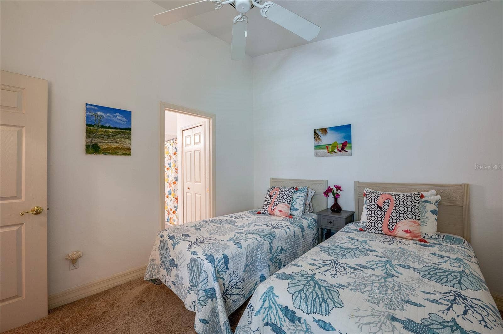 Inviting bedroom layout framed by soft neutral walls, high ceilings, and plush carpeting. An open doorway offers direct access to an adjacent full bathroom.