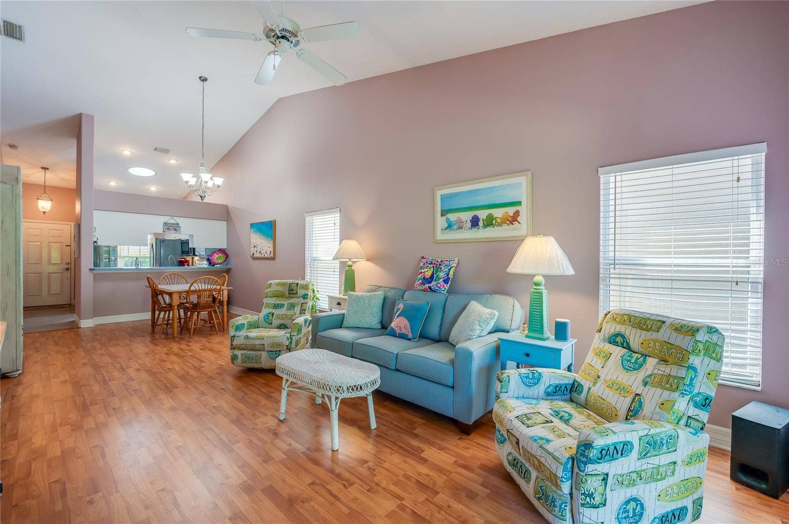 Expansive open-concept main living area defined by high ceilings and continuous laminate flooring. Large windows flood the space with natural light, connecting the front entry, kitchen pass-through, and living space.