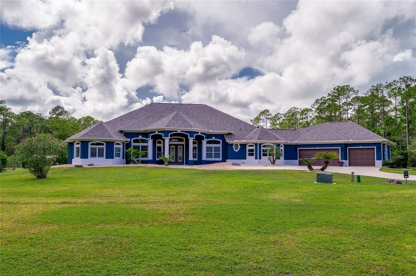 25 REMINGTON ROAD, Ormond Beach, FL 32174 Front exterior shot of the blue home showing distinct architectural rooflines, columns, and a multi-car garage.