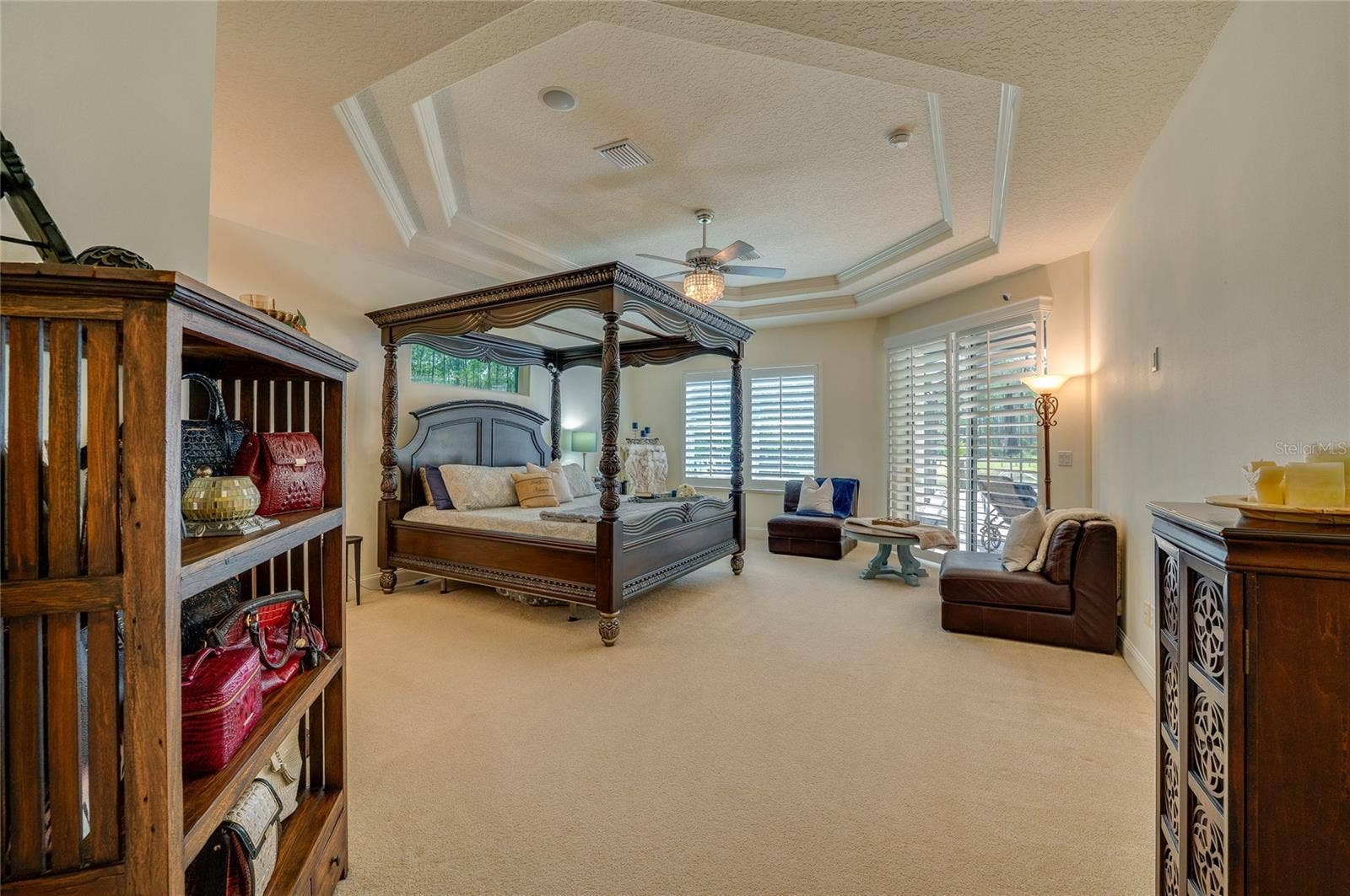 25 REMINGTON ROAD, Ormond Beach, FL 32174 Spacious primary bedroom suite showcasing neutral carpet, a tray ceiling with a ceiling fan, and large windows leading toward the outdoor patio.