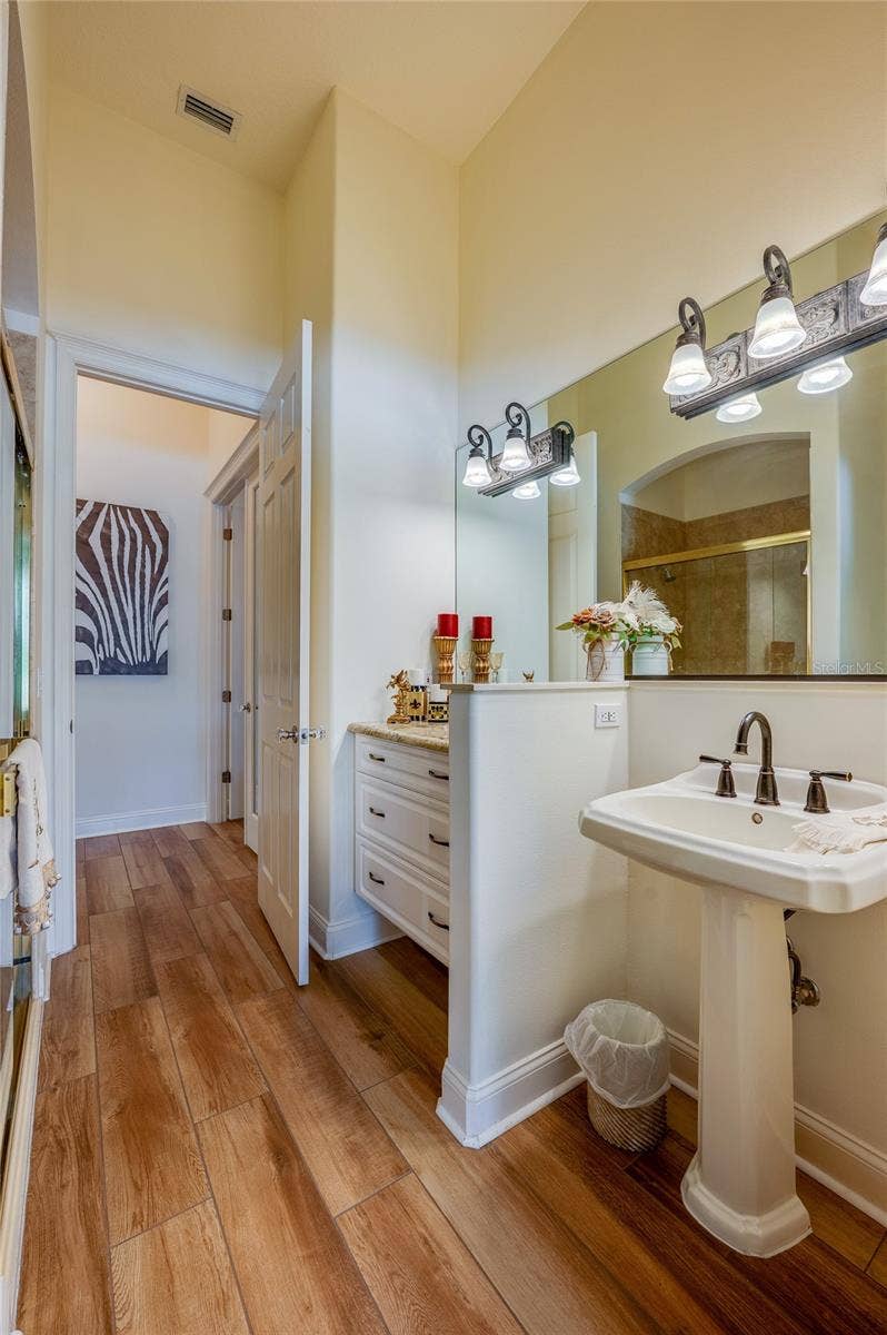 25 REMINGTON ROAD, Ormond Beach, FL 32174 Light-filled bathroom space with tile flooring, a pedestal sink, framed mirror with vanity lighting, and open hallway access.
