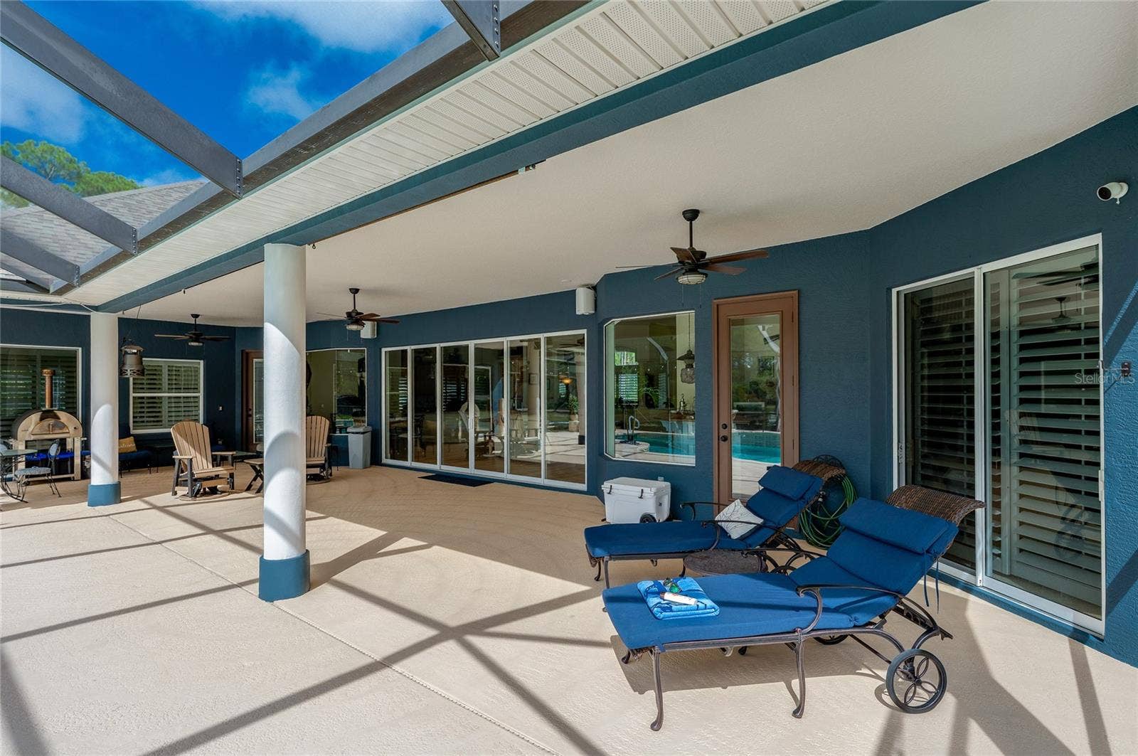 25 REMINGTON ROAD, Ormond Beach, FL 32174 Sheltered porch area with ceiling fans, dark blue exterior walls, and sliding glass doors that open to the interior living space.