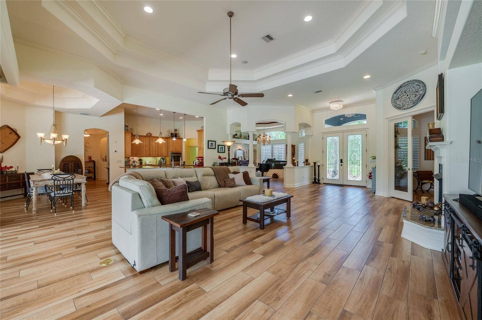 25 REMINGTON ROAD, Ormond Beach, FL 32174 Sunlit main living room featuring high double-tray ceilings with a ceiling fan, tile flooring throughout, and immediate access to the entryway.