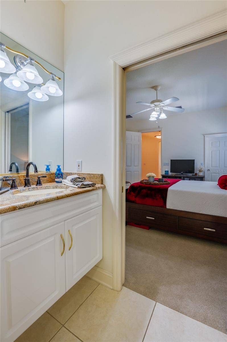 25 REMINGTON ROAD, Ormond Beach, FL 32174 Convenient en-suite bathroom featuring a granite vanity, vanity lighting, and tiled flooring, providing seamless access into the adjoining bedroom.