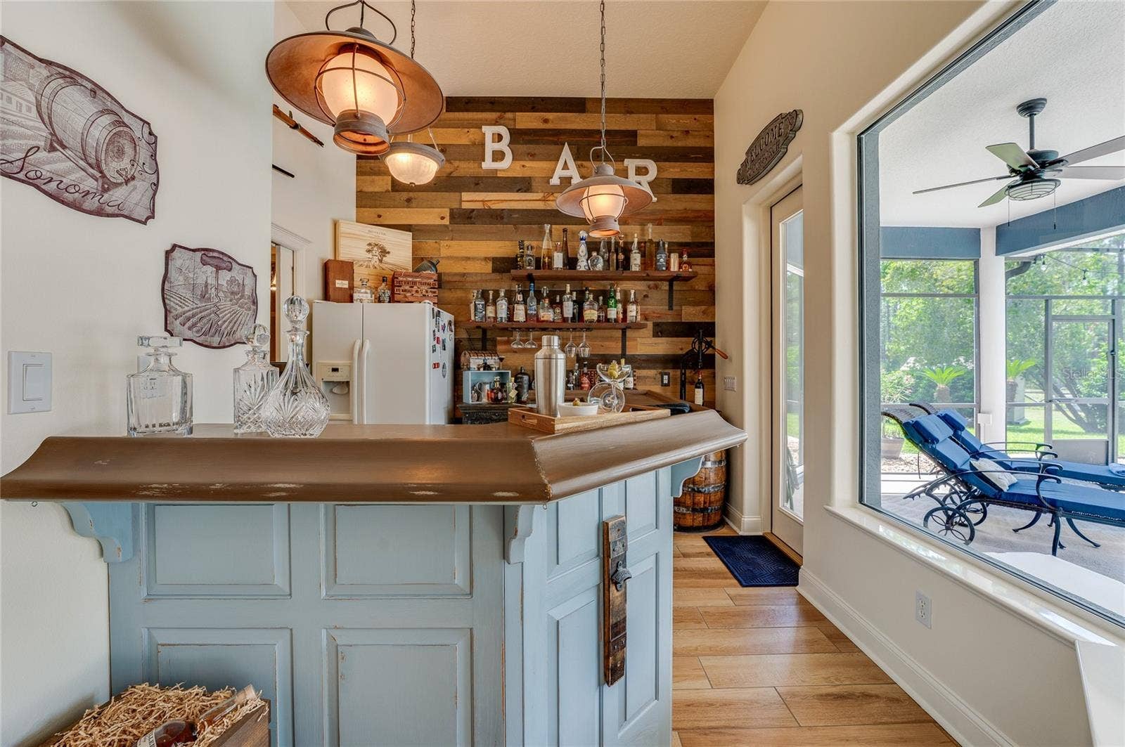 25 REMINGTON ROAD, Ormond Beach, FL 32174 Rustic home bar setup featuring wood-paneled accent walls, integrated shelving, hanging pendant lights, and a view into the adjacent screened patio.