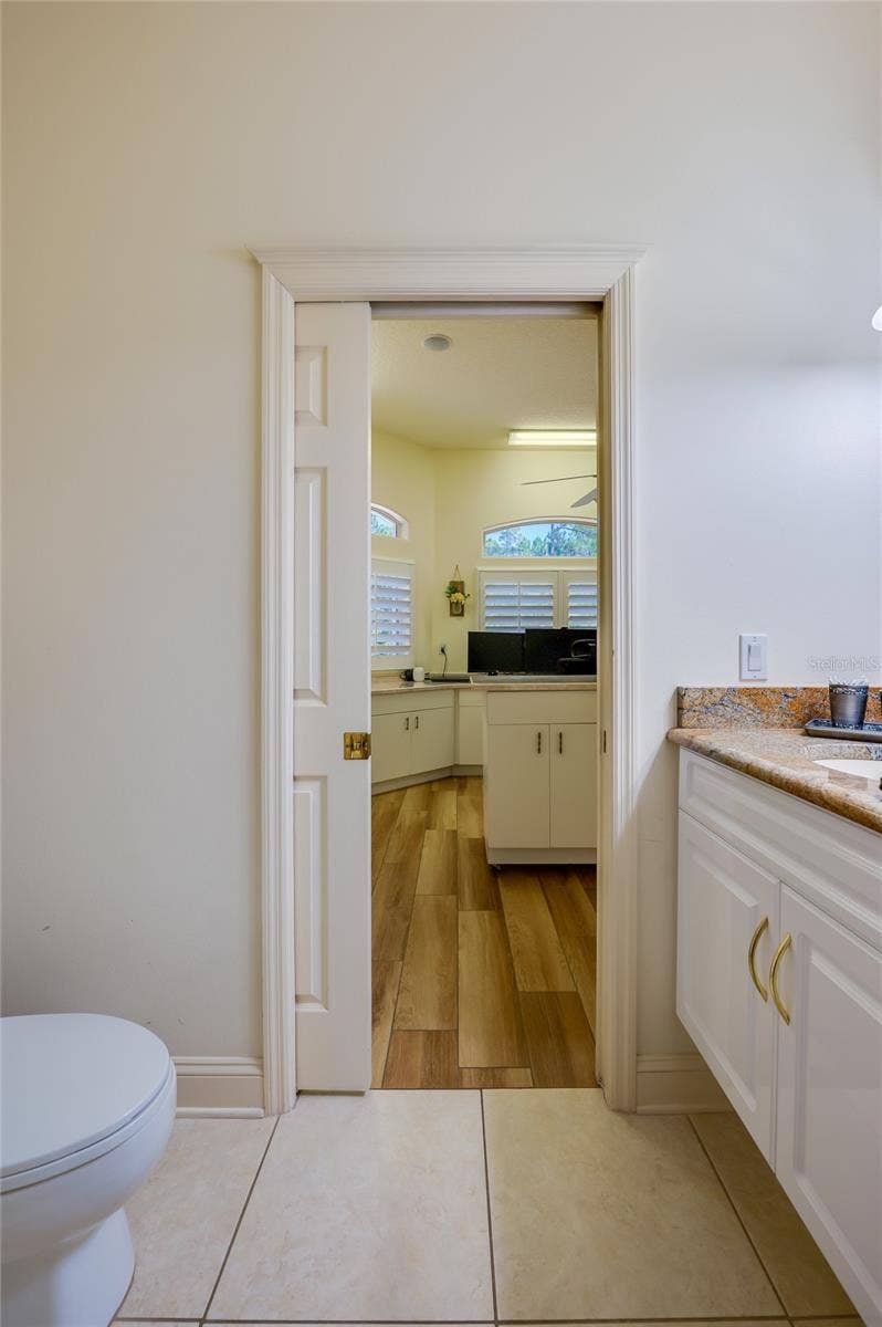 25 REMINGTON ROAD, Ormond Beach, FL 32174 Functional bathroom area featuring a white vanity with granite countertops, light tile flooring, and a pocket door opening into an adjoining room.