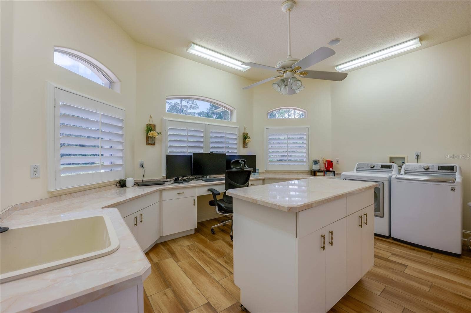 25 REMINGTON ROAD, Ormond Beach, FL 32174 Bright laundry and workspace hub offering abundant counter space, built-in storage cabinets, window shutters, and overhead lighting.