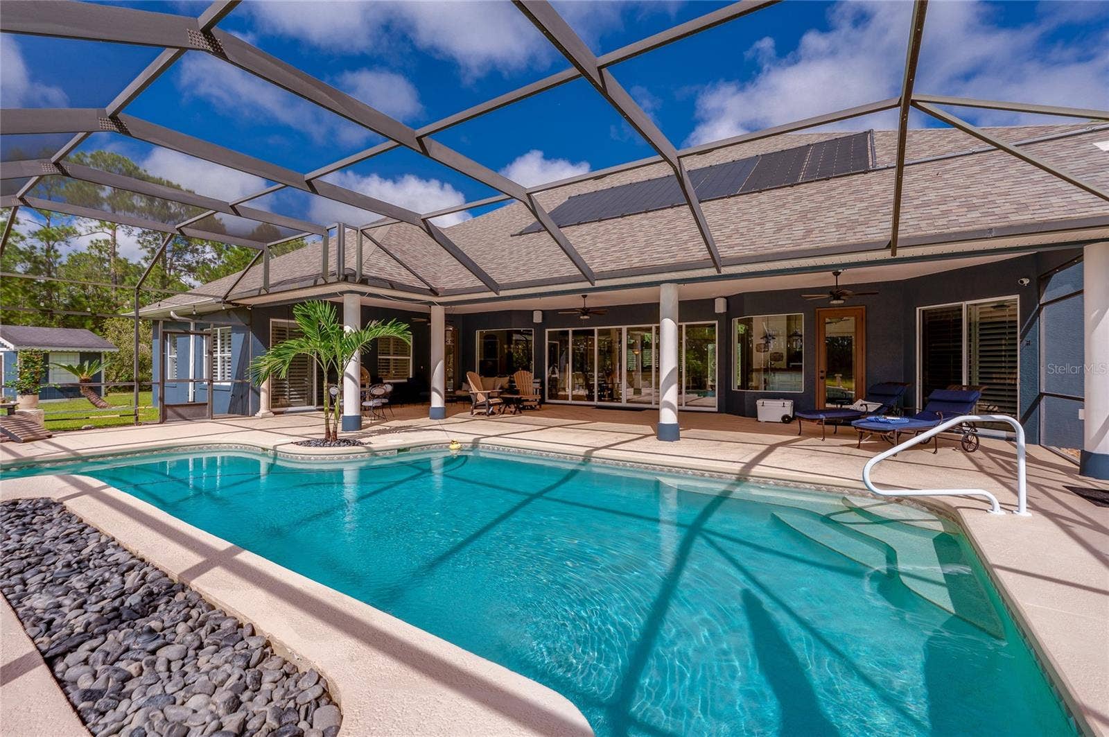 25 REMINGTON ROAD, Ormond Beach, FL 32174 Overview of the screened pool enclosure showcasing roof-mounted solar panels and wide steps leading into the pool.