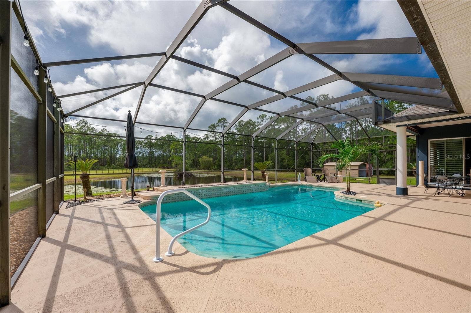 25 REMINGTON ROAD, Ormond Beach, FL 32174 Screened-in pool deck featuring a crystal-clear swimming pool, integrated handrail, and views of the private backyard pond.