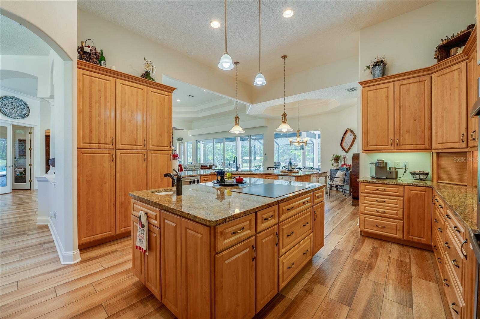 25 REMINGTON ROAD, Ormond Beach, FL 32174 Expansive kitchen layout showcasing a massive granite-topped island with cooktop, prep sink, and surrounding tall storage cabinets.