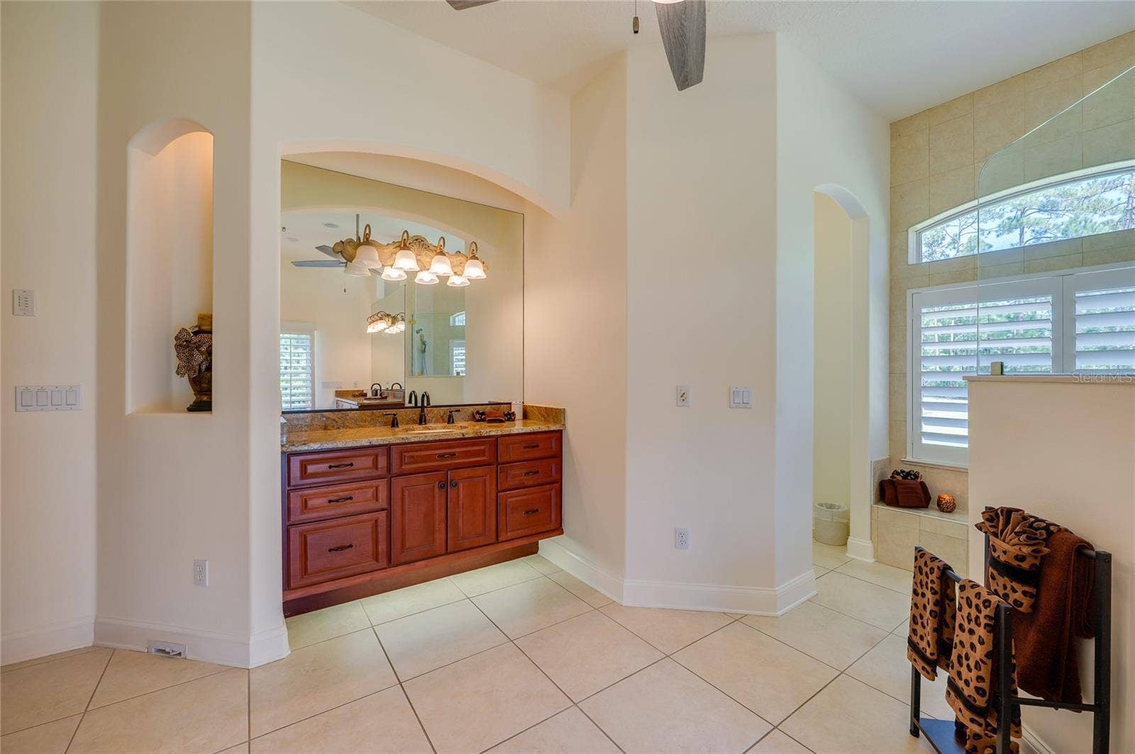 25 REMINGTON ROAD, Ormond Beach, FL 32174 Open bathroom alcove highlighting light tile floors, a wooden vanity with granite counter, and arched architectural details leading into separate shower and toilet areas.