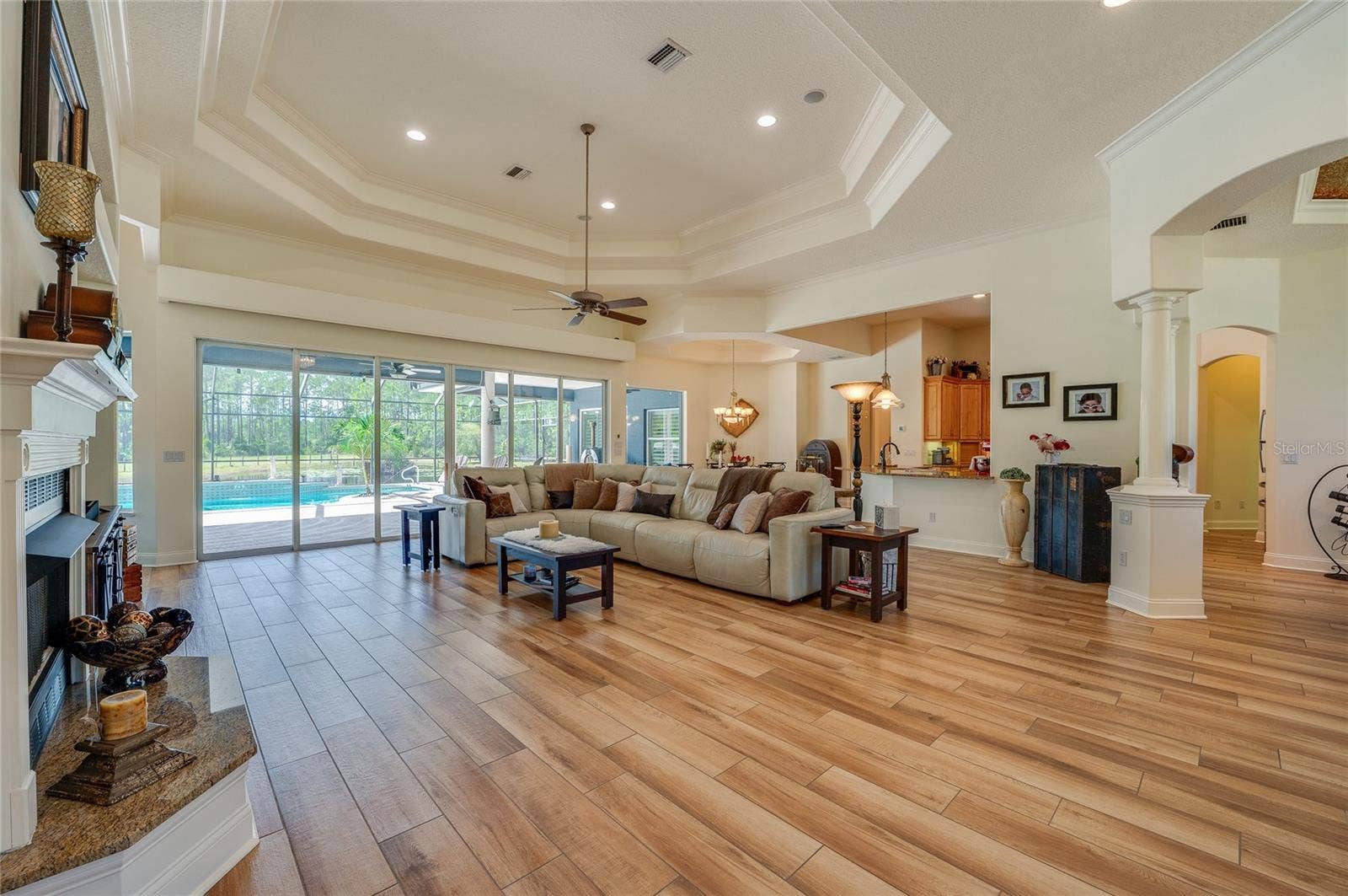 25 REMINGTON ROAD, Ormond Beach, FL 32174 Spacious open floor plan showcasing high multi-tier tray ceilings, a built-in fireplace, and large sliding glass doors opening up to the screened pool patio.