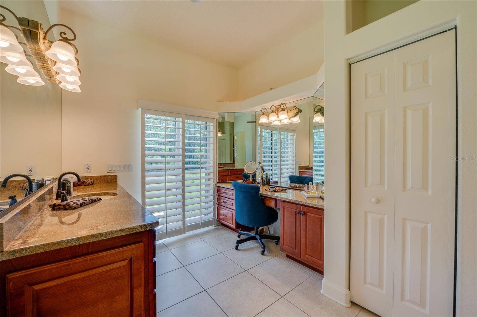 25 REMINGTON ROAD, Ormond Beach, FL 32174 Well-lit bathroom vanity nook featuring granite countertops, extensive mirror paneling, and window shutters providing natural light.