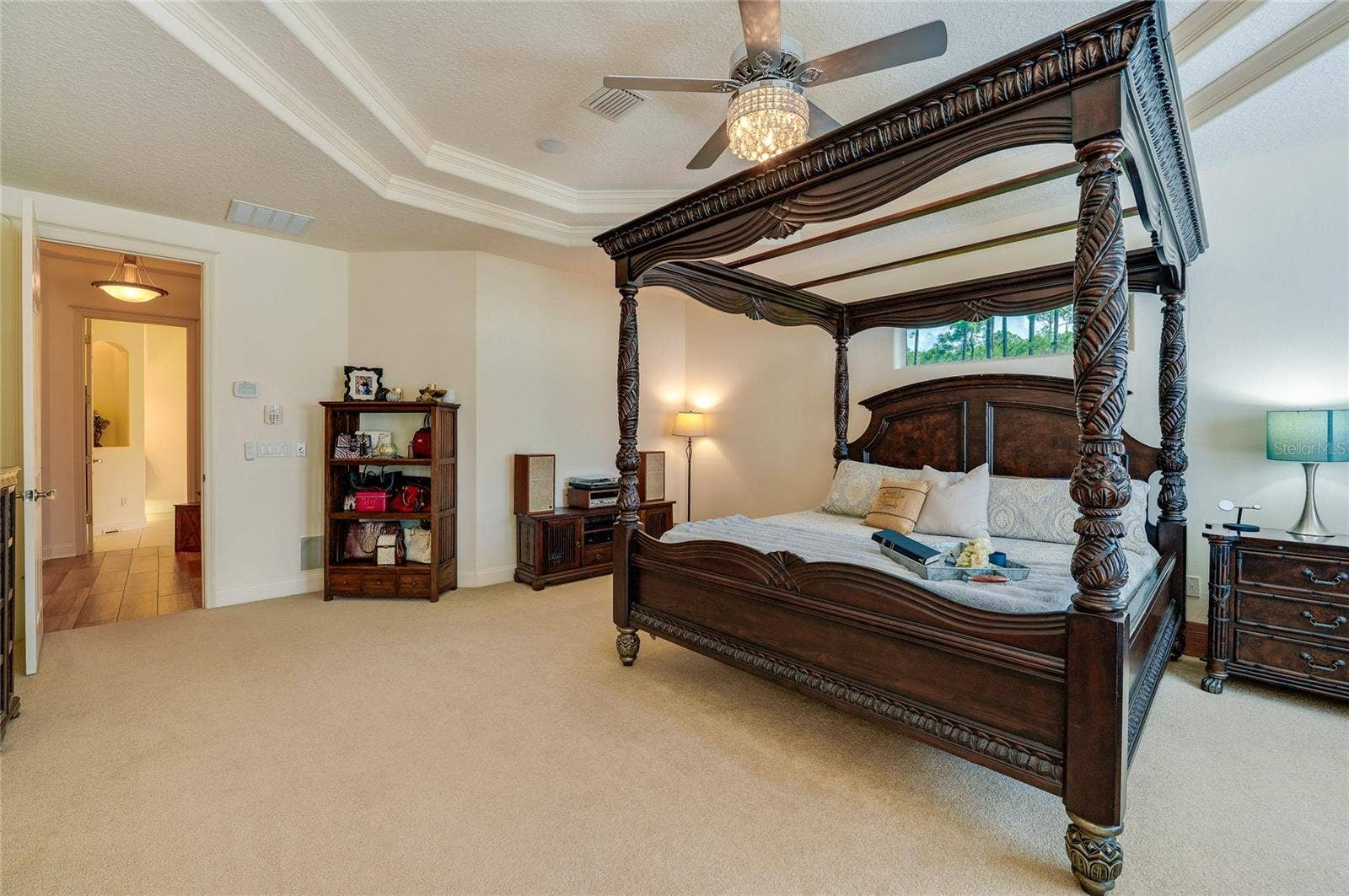 25 REMINGTON ROAD, Ormond Beach, FL 32174 Primary bedroom layout featuring a layered tray ceiling, elegant fan fixture, neutral carpeting, and an adjacent private entryway.