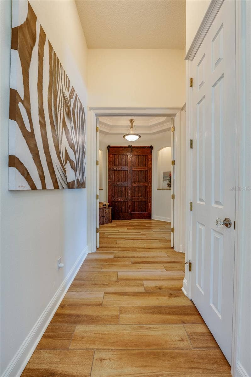 25 REMINGTON ROAD, Ormond Beach, FL 32174 Bright interior hallway displaying tile floors, high ceilings, white trim, and views leading toward rustic double barn doors.