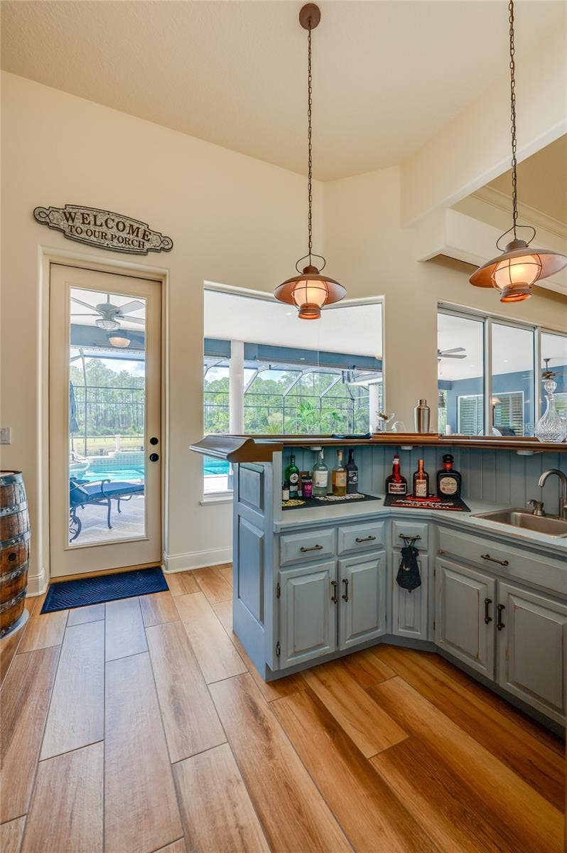 25 REMINGTON ROAD, Ormond Beach, FL 32174 Functional wet bar equipped with built-in cabinetry, prep sink, and overhead pendant lights near a glass door leading to the outdoor pool area.
