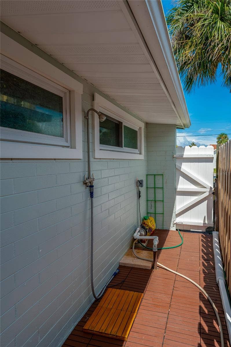 348 WOODLAND AVENUE, Daytona Beach, FL 32118 Convenient outdoor shower station installed along the side exterior wall with a wooden foot mat. A white vinyl gate provides privacy and secure access to the yard.