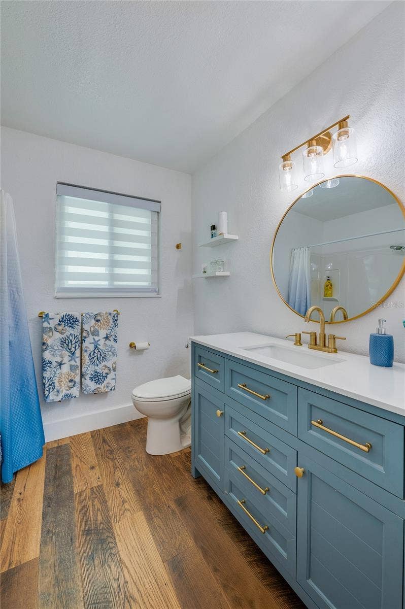 348 WOODLAND AVENUE, Daytona Beach, FL 32118 Stylish bathroom featuring a blue vanity with gold hardware, a round brass-framed mirror, and modern lighting.