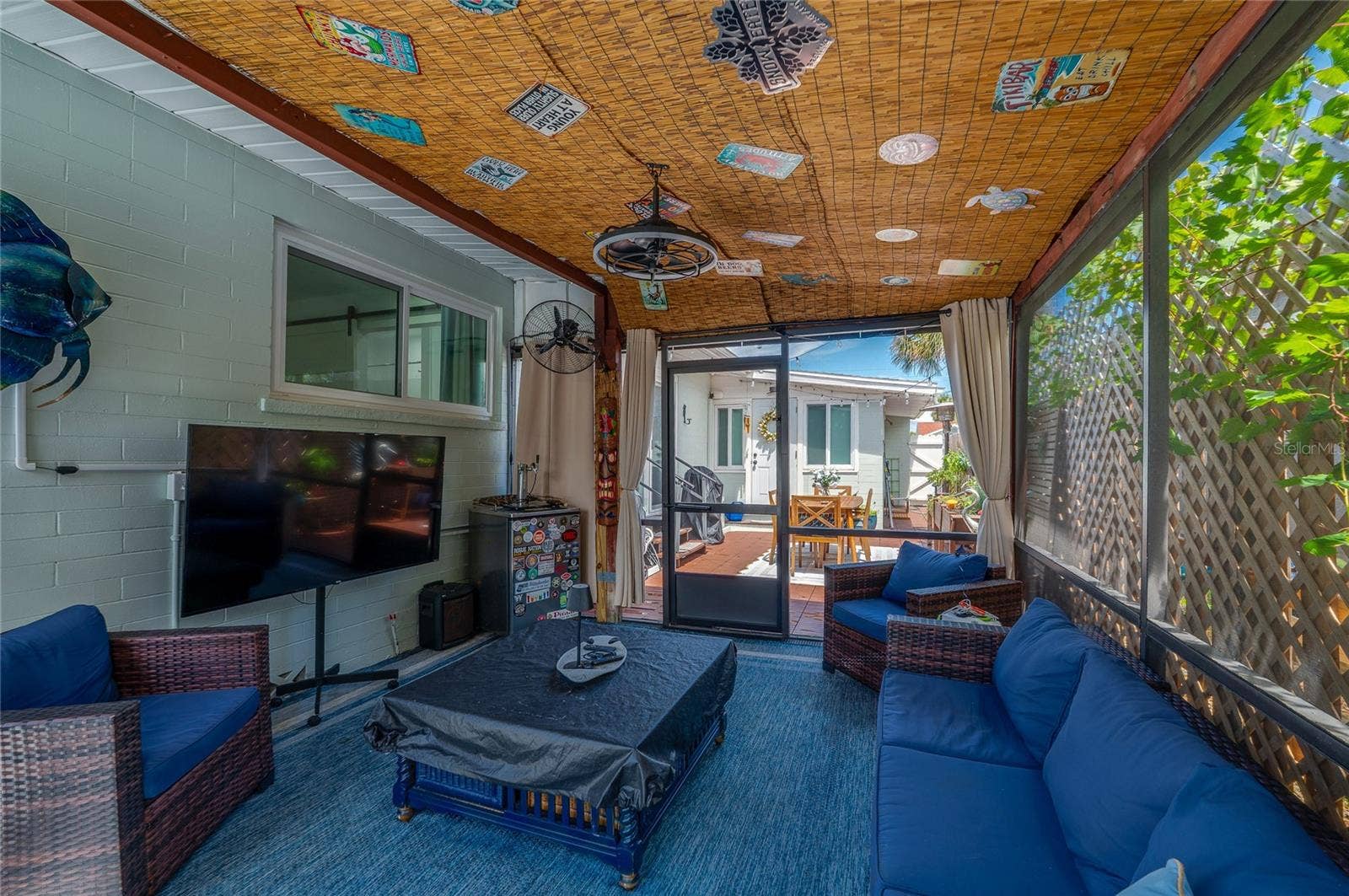 348 WOODLAND AVENUE, Daytona Beach, FL 32118 Inviting screened-in patio area with decorative bamboo ceiling panels and sheer privacy curtains. It offers clear views leading out to the sunlit outdoor deck.