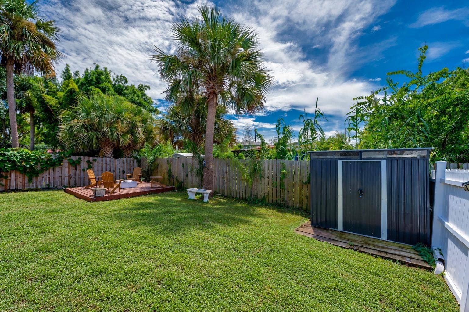 348 WOODLAND AVENUE, Daytona Beach, FL 32118 Fenced backyard area featuring a standalone storage shed and mature palm trees. A raised wooden platform sits tucked in the corner of the yard.