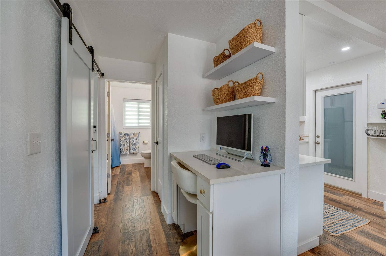 348 WOODLAND AVENUE, Daytona Beach, FL 32118 Built-in study alcove with white cabinetry, quartz counter space, and floating shelves, situated in a hallway featuring LVP floors and a sliding barn door.