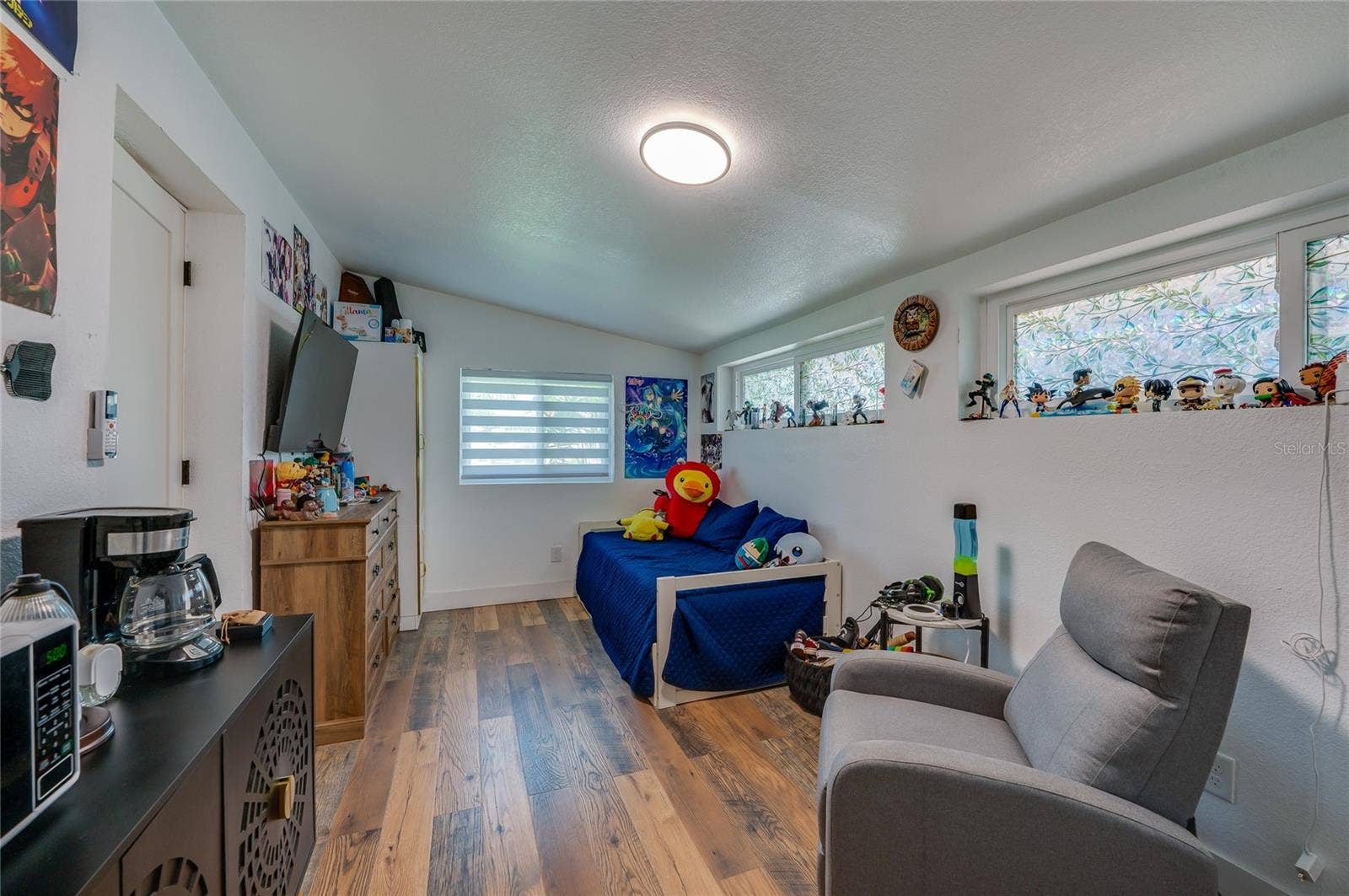 348 WOODLAND AVENUE, Daytona Beach, FL 32118 Cozy bedroom featuring LVP flooring, sloped ceilings, ample natural light from multiple windows, and smooth neutral walls.