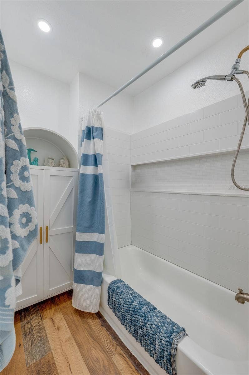 348 WOODLAND AVENUE, Daytona Beach, FL 32118 Updated bathroom display showing a white shower surround with built-in storage niches, brushed gold shower fixtures, and a white arched storage cabinet.