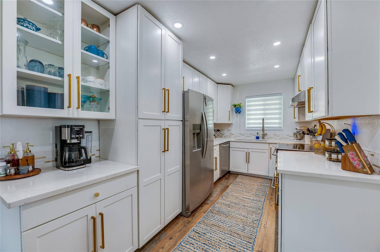 348 WOODLAND AVENUE, Daytona Beach, FL 32118 Gourmet galley kitchen featuring crisp white shaker cabinetry, gold hardware accents, stainless steel appliances, and quartz countertops.