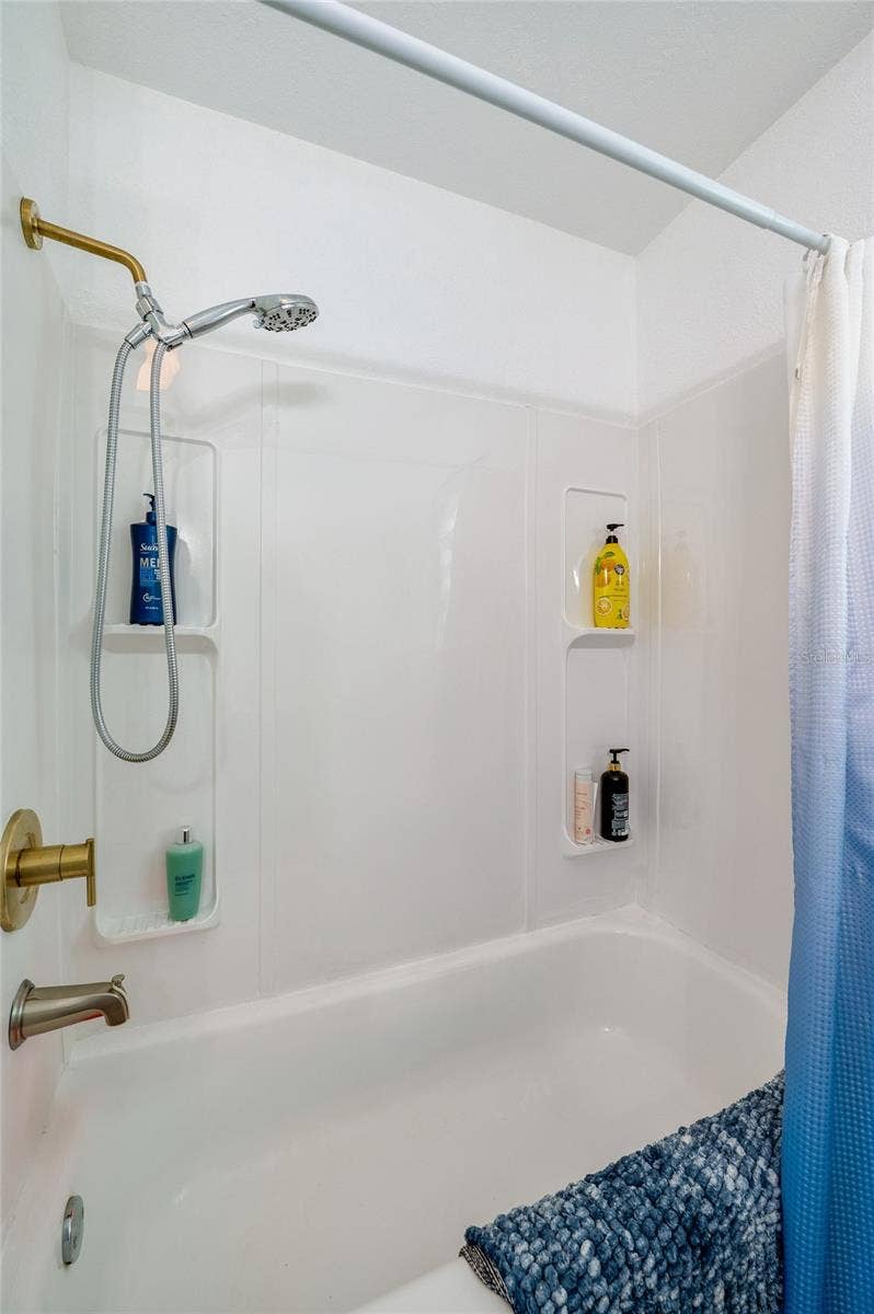 348 WOODLAND AVENUE, Daytona Beach, FL 32118 Close-up of a updated bathtub and shower combination complete with a white surround, dual wall niches for toiletries, and warm gold hardware.