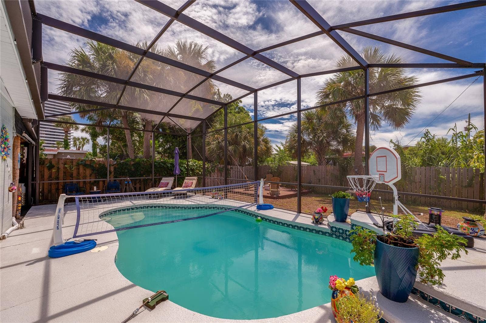348 WOODLAND AVENUE, Daytona Beach, FL 32118 In-ground swimming pool inside a fully screened enclosure. Tiled accents and potted plants border the sunlit pool deck.