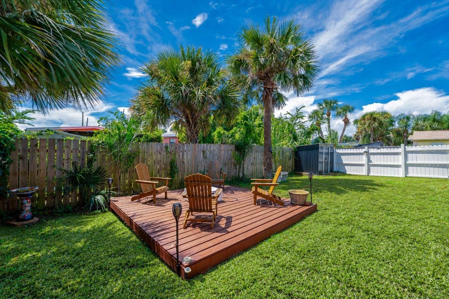 348 WOODLAND AVENUE, Daytona Beach, FL 32118 Raised wooden deck platform set within a private, fully fenced backyard. Tall palm trees overhead provide natural shade and tropical ambiance.