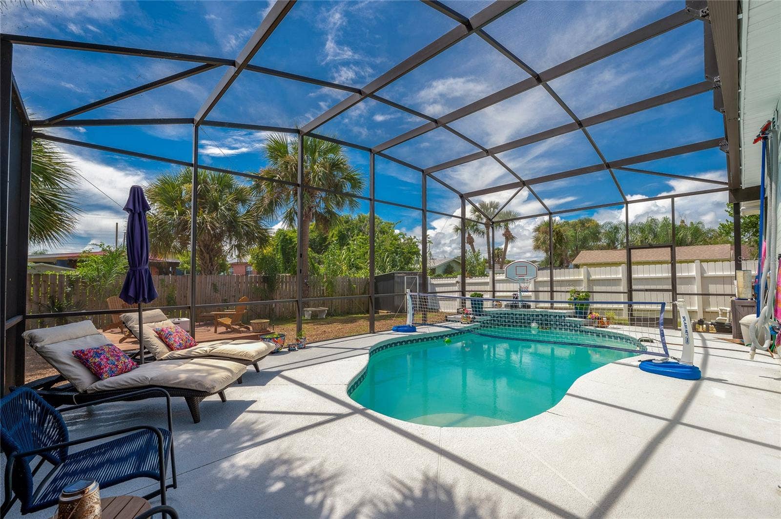 348 WOODLAND AVENUE, Daytona Beach, FL 32118 Fully screened pool enclosure featuring a crystal-clear swimming pool. Lush palm trees and a wooden fence surround the perimeter for privacy.