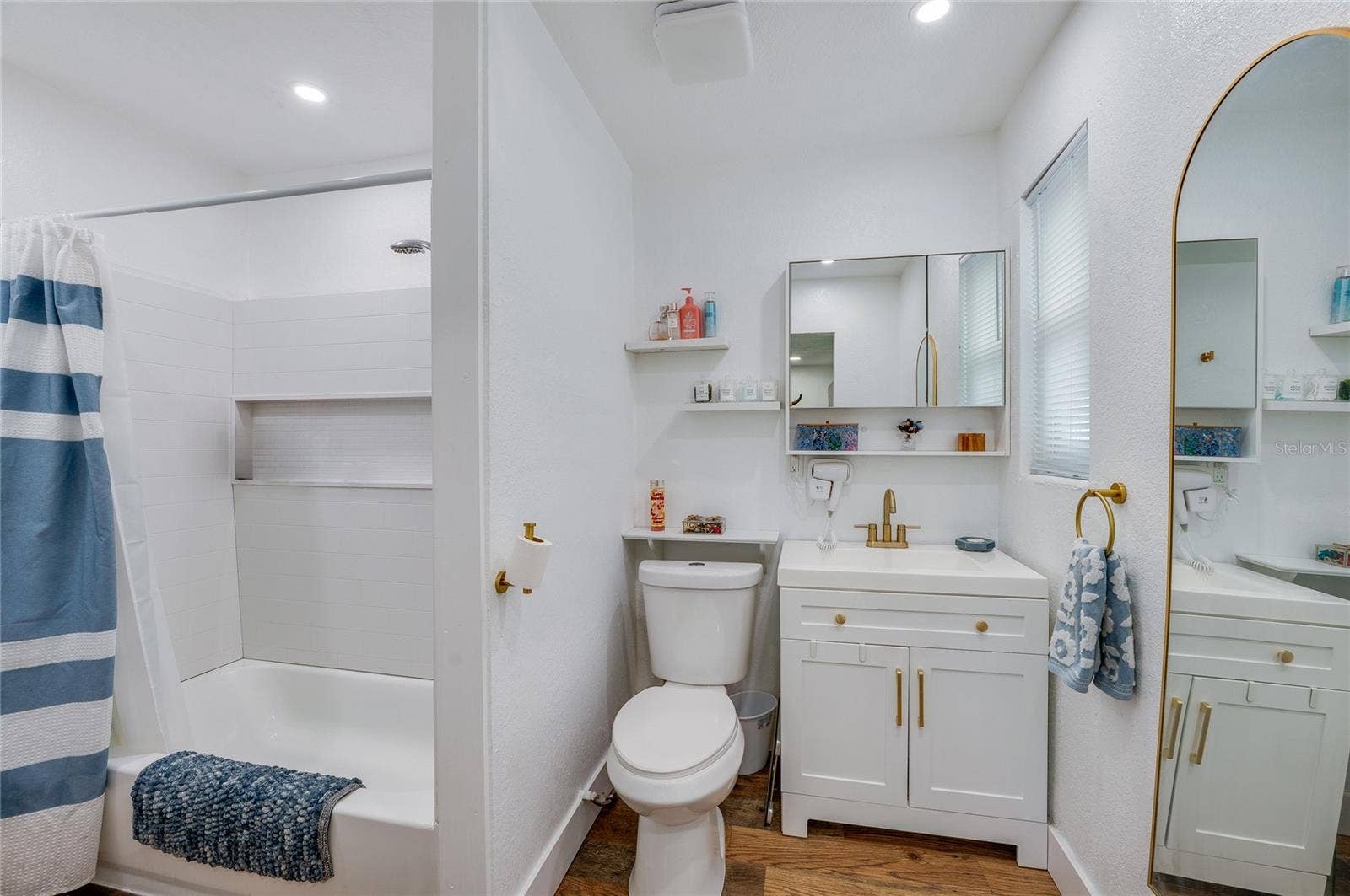 348 WOODLAND AVENUE, Daytona Beach, FL 32118 Clean full bathroom featuring a white vanity with gold hardware accents, LVP flooring, and a tub shower combination.